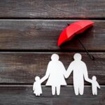 Live insurance concept. Family silhouette protected by umbrella on dark wooden background top-down copy space